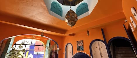 Una habitación con una lámpara octogonal grande en el techo, una mesa redonda con sillas, un sofá y vistas al exterior a través de un arco.