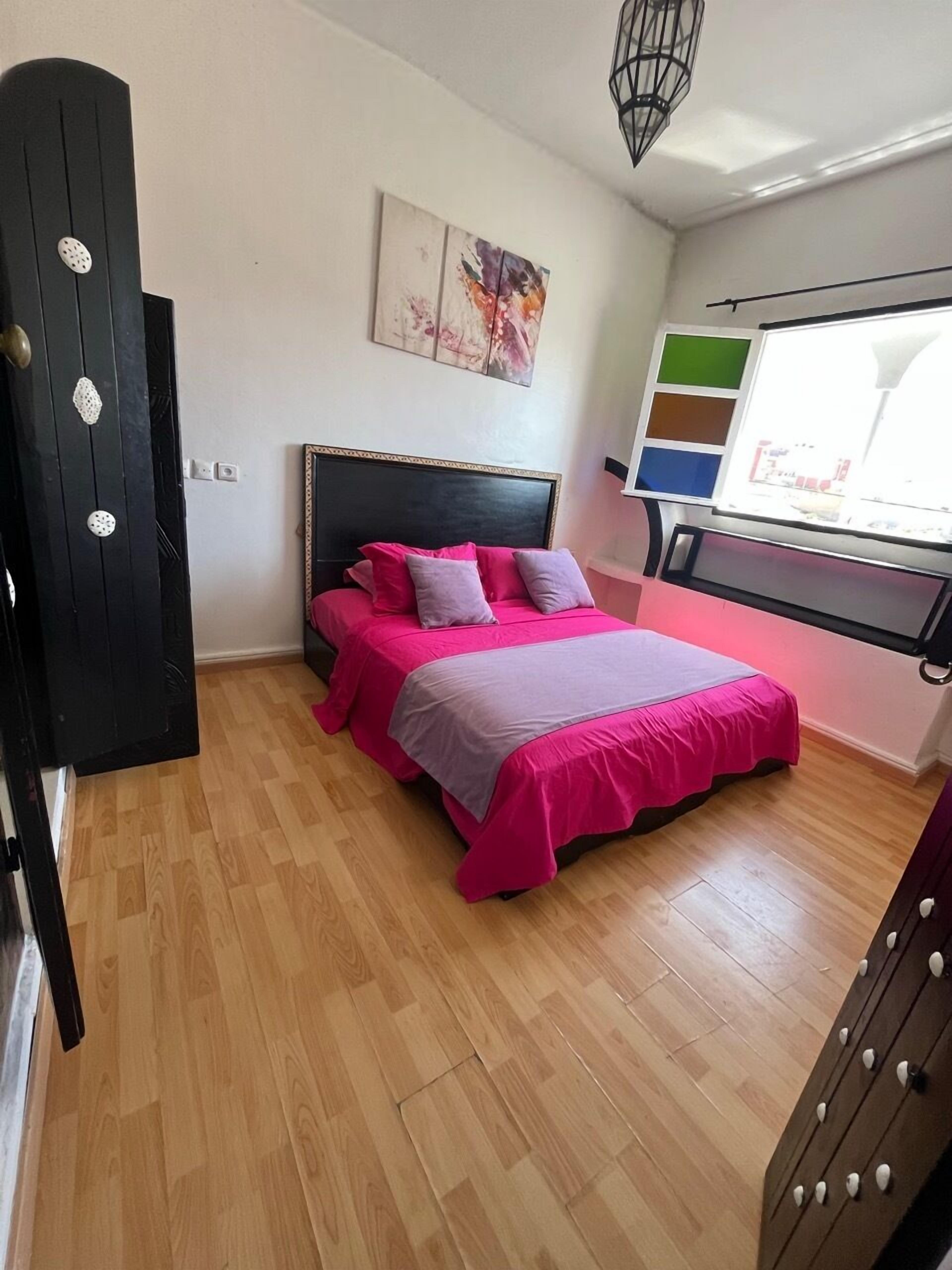 Un dormitorio con una cama, una ventana con persianas, un cuadro en la pared y una puerta.