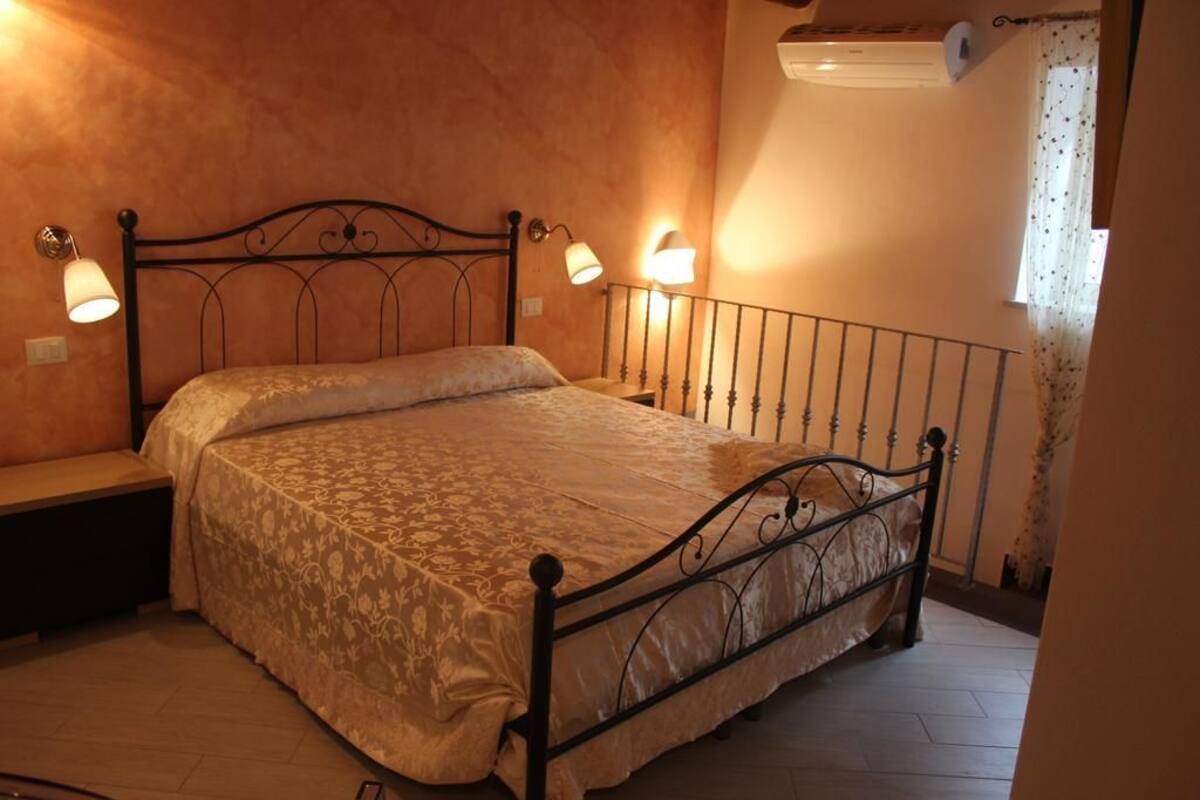 A bedroom with a metal bed frame, two bedside lamps, a bench, and a window with curtains.