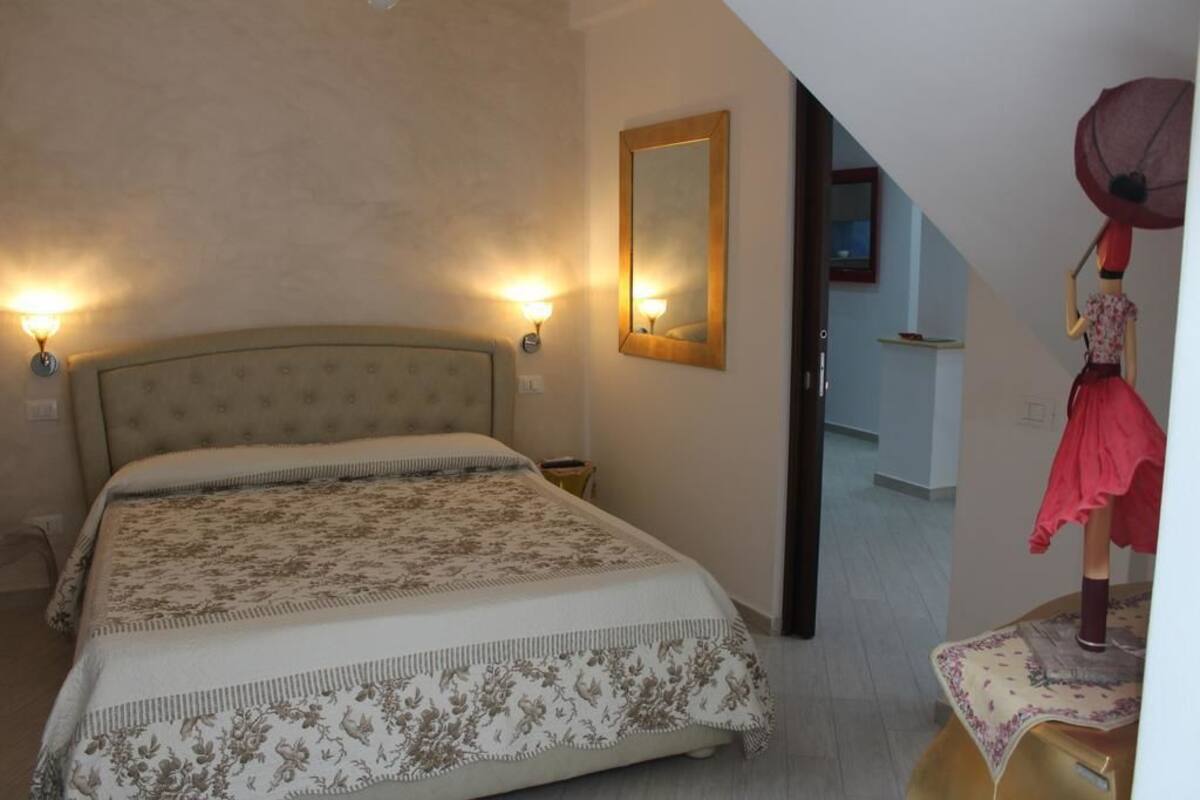 A bedroom with a large bed, two wall-mounted lights, a mirror, and a mannequin with a red dress.