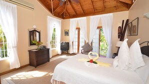 Una habitación de hotel con techo de madera, una cama con ropa blanca, un televisor, un aparador y una ventana con cortinas.