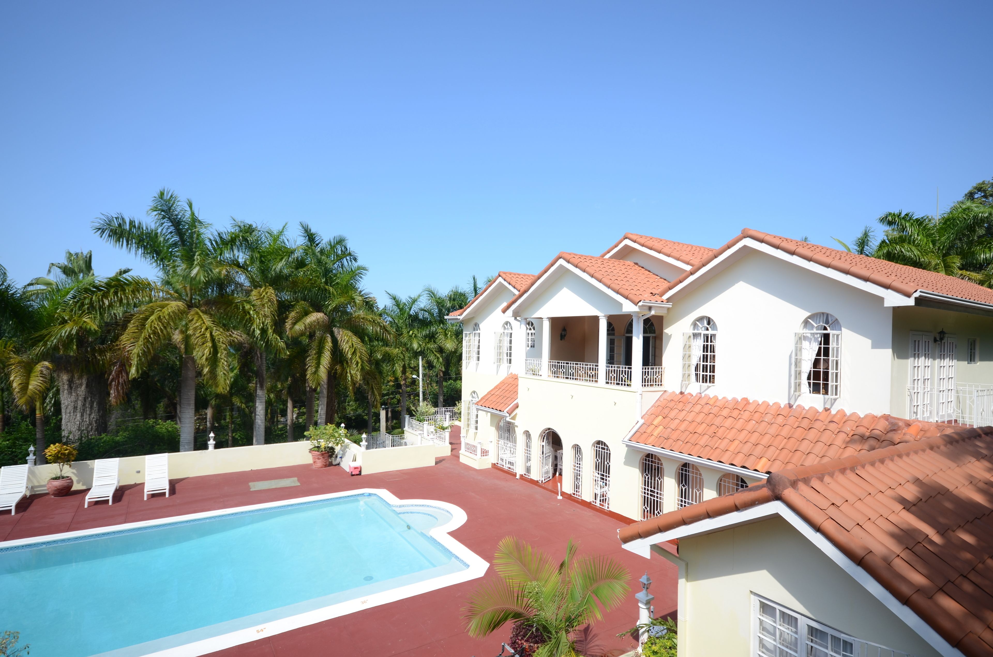 A large white building with a swimming pool, surrounded by palm trees.