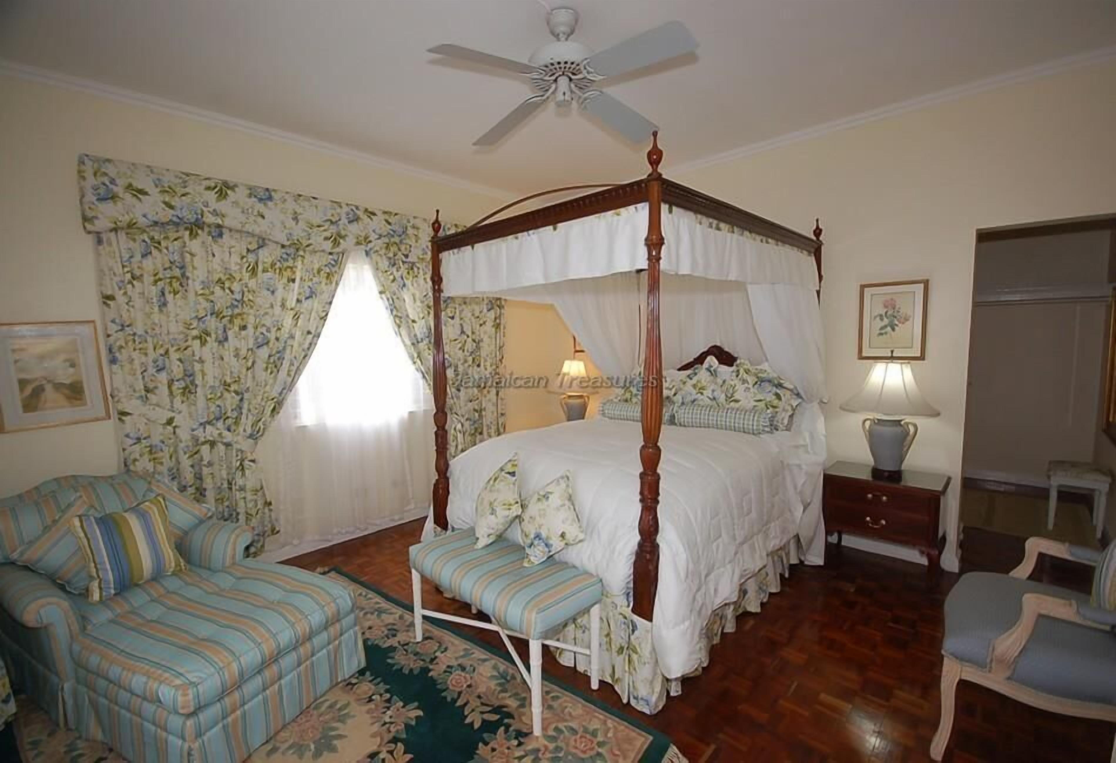 A bedroom with a four-poster bed, a sofa, a bench, a nightstand, and a chair.