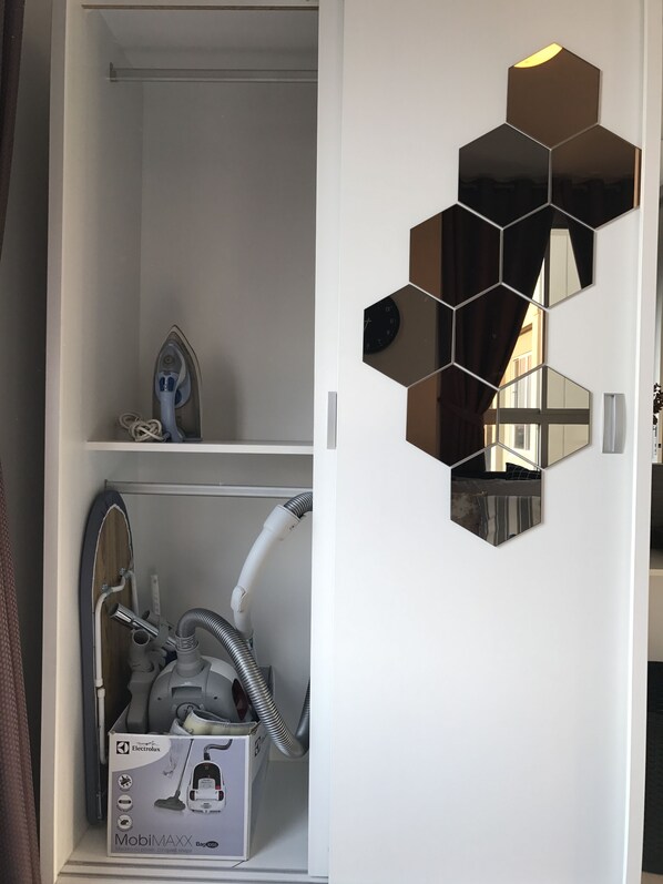 A bathroom with a white door, a mirror with hexagonal frames, and a shower area with a handheld showerhead and a white box labeled "Electrolux MobilMAX Bag 85".