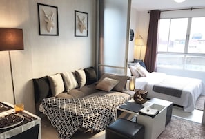 A hotel room with a bed, a sofa, a desk, and a dining table. There are two framed deer heads on the wall, a clock, and a window with curtains.