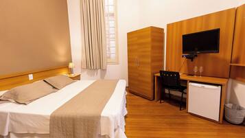 Una habitación de hotel con cama, escritorio con computadora, televisor y refrigerador pequeño.