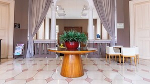 Un vestíbulo con una mesa redonda de madera, una planta en maceta y una zona de estar con sillas blancas.