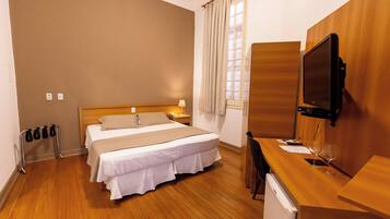 A hotel room with a bed, bedside table, TV, and a desk with a chair.