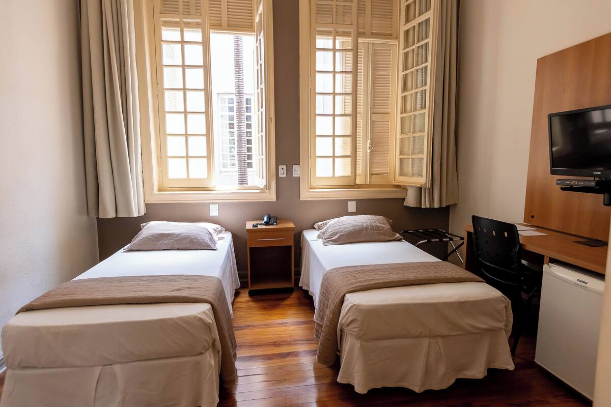 A hotel room with two single beds, a small bedside table with a lamp, a TV, and a mini-fridge.