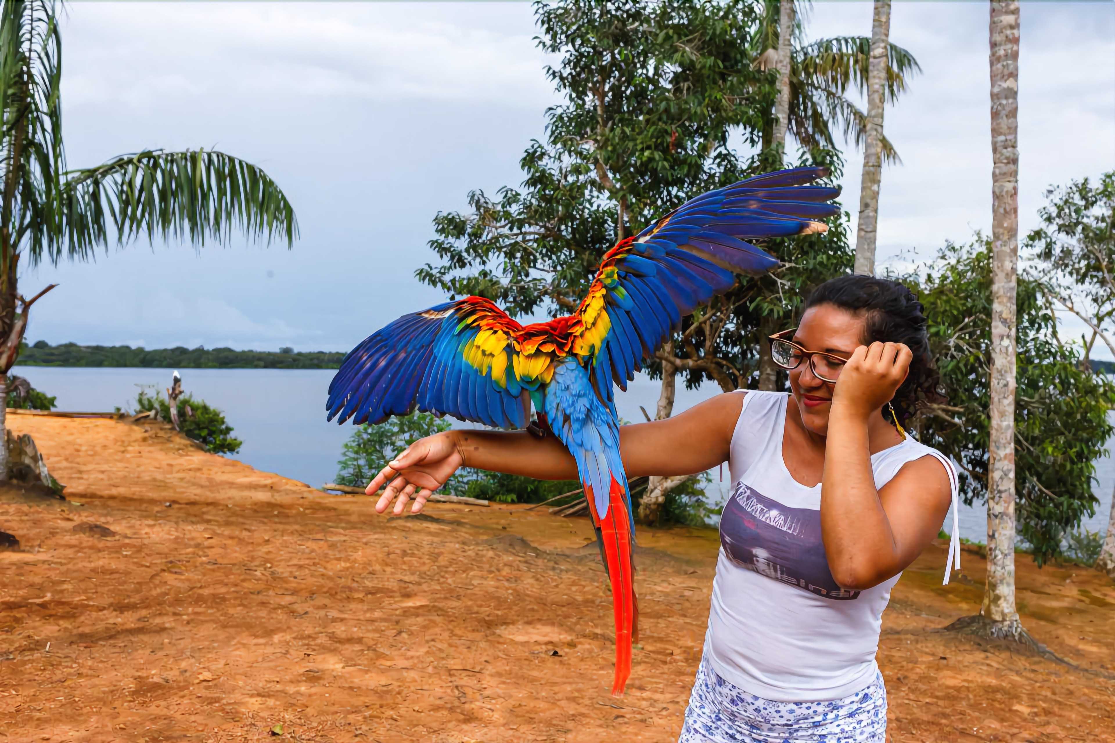 A person holding a colorful parrot with outstretched wings.