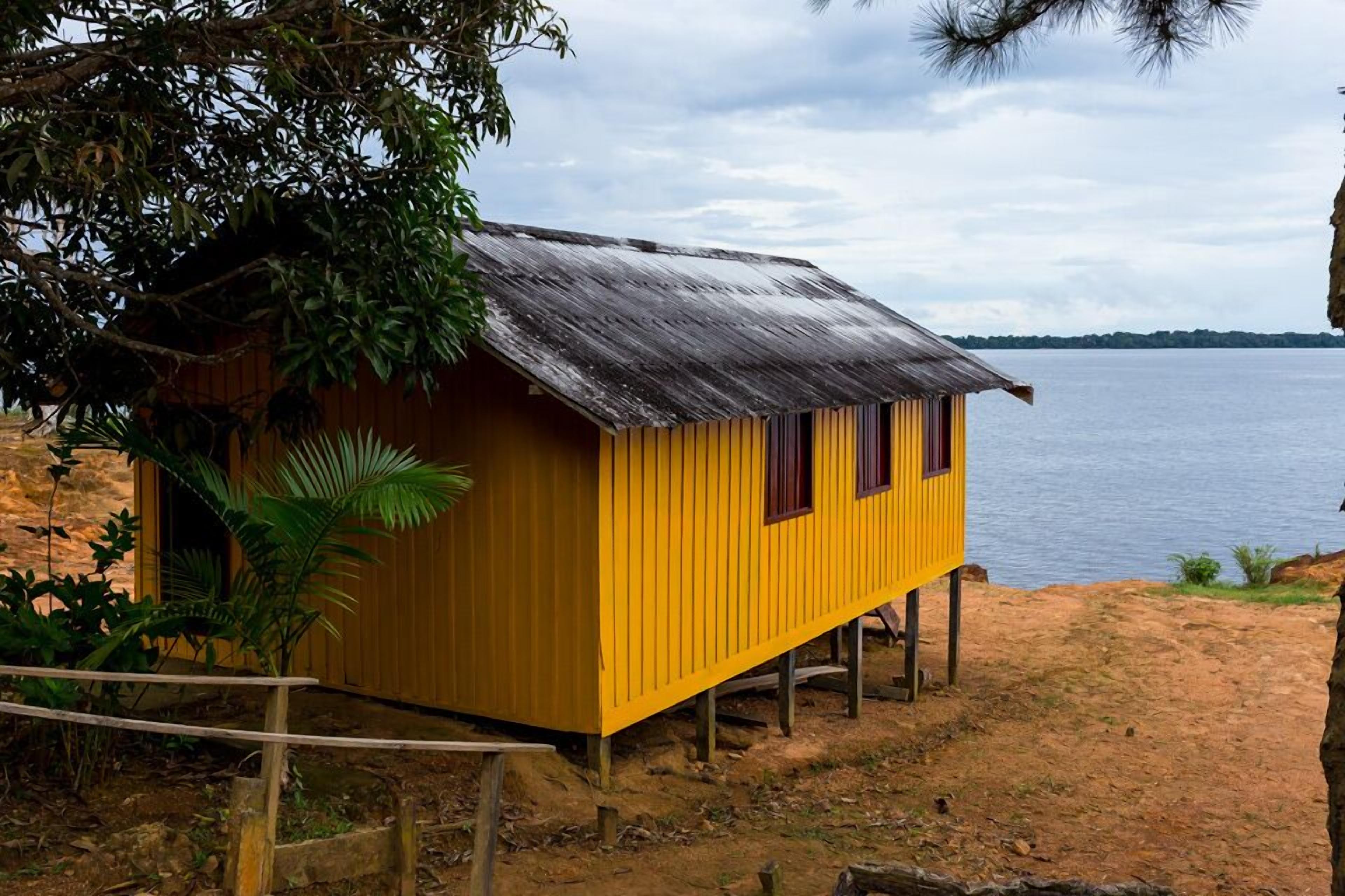 A yellow wooden structure with a metal roof, situated on a sandy beach with a body of water in the background.