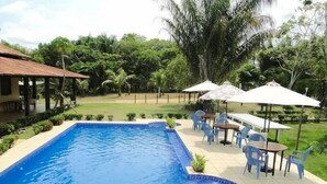 A swimming pool with a hot tub, surrounded by outdoor seating and umbrellas, set in a lush garden with a house in the background. - Amazônia ParkSuítes (Novo Airão)
