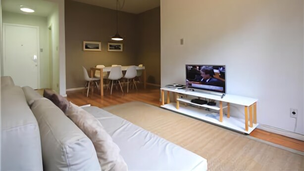 Ein Wohnzimmer mit Sofa, Esstisch, Stühlen und einem Fernseher auf einem Schrank.