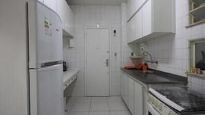 Eine schmale Küche mit weißen Schränken, einem Kühlschrank, einem Herd und einem Spülbecken.