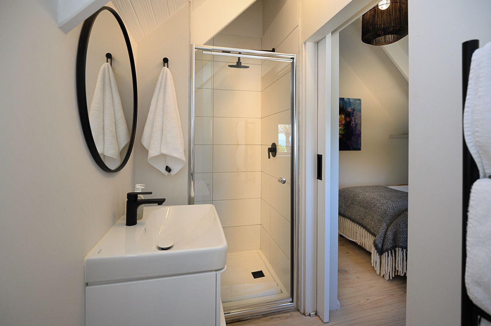 Ein modernes Badezimmer mit Duschkabine aus Glas, einem weißen Waschbecken und zwei Handtüchern, die an der Wand hängen.