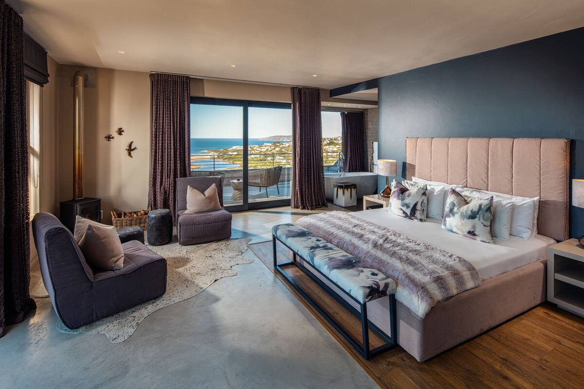 Un dormitorio moderno con una cama grande, un sofá, una silla y vistas al mar.