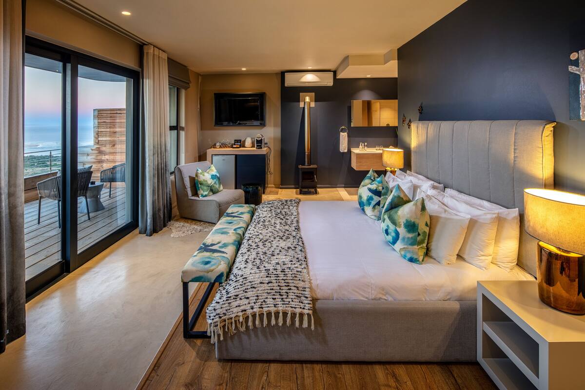Habitación de hotel moderna con una cama grande, un banco, un escritorio y vista al océano.