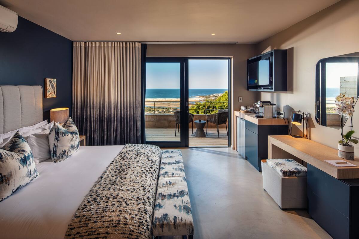 Una habitación de hotel moderna con una cama grande, un escritorio, un televisor y un balcón con vistas a la playa.