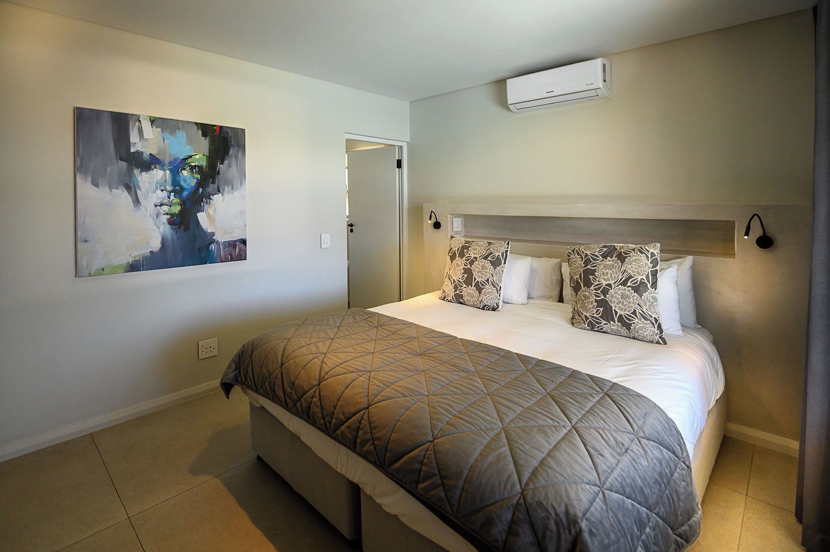Un dormitorio con una cama, un cuadro en la pared, un equipo de aire acondicionado y una puerta.