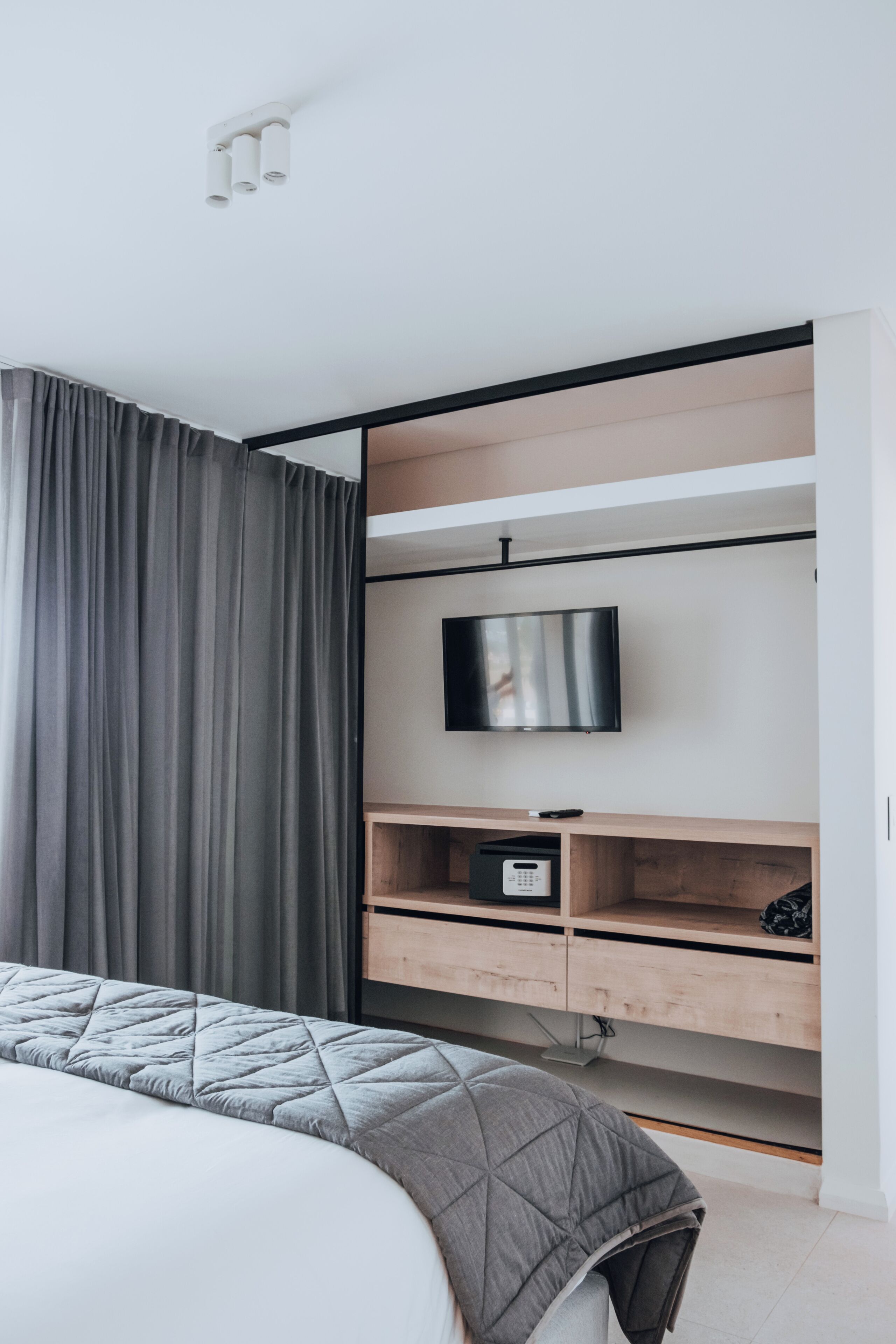 Un dormitorio moderno con una cama, un televisor fijado a una repisa de madera y un panel de control.