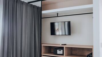 Un dormitorio moderno con una cama, un televisor fijado a una repisa de madera y un panel de control.
