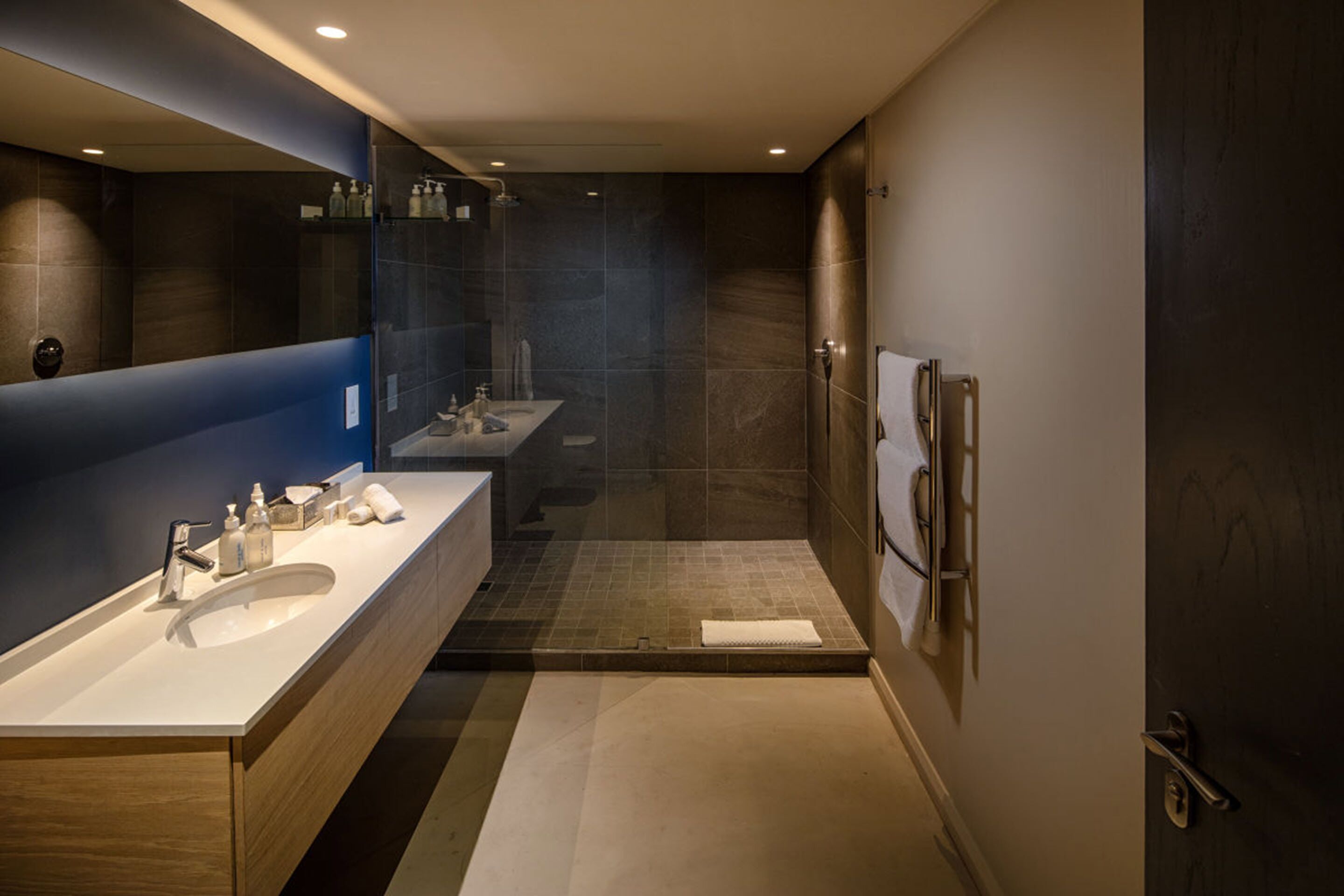 Een moderne badkamer met twee wastafels, een douche en een grote spiegel.