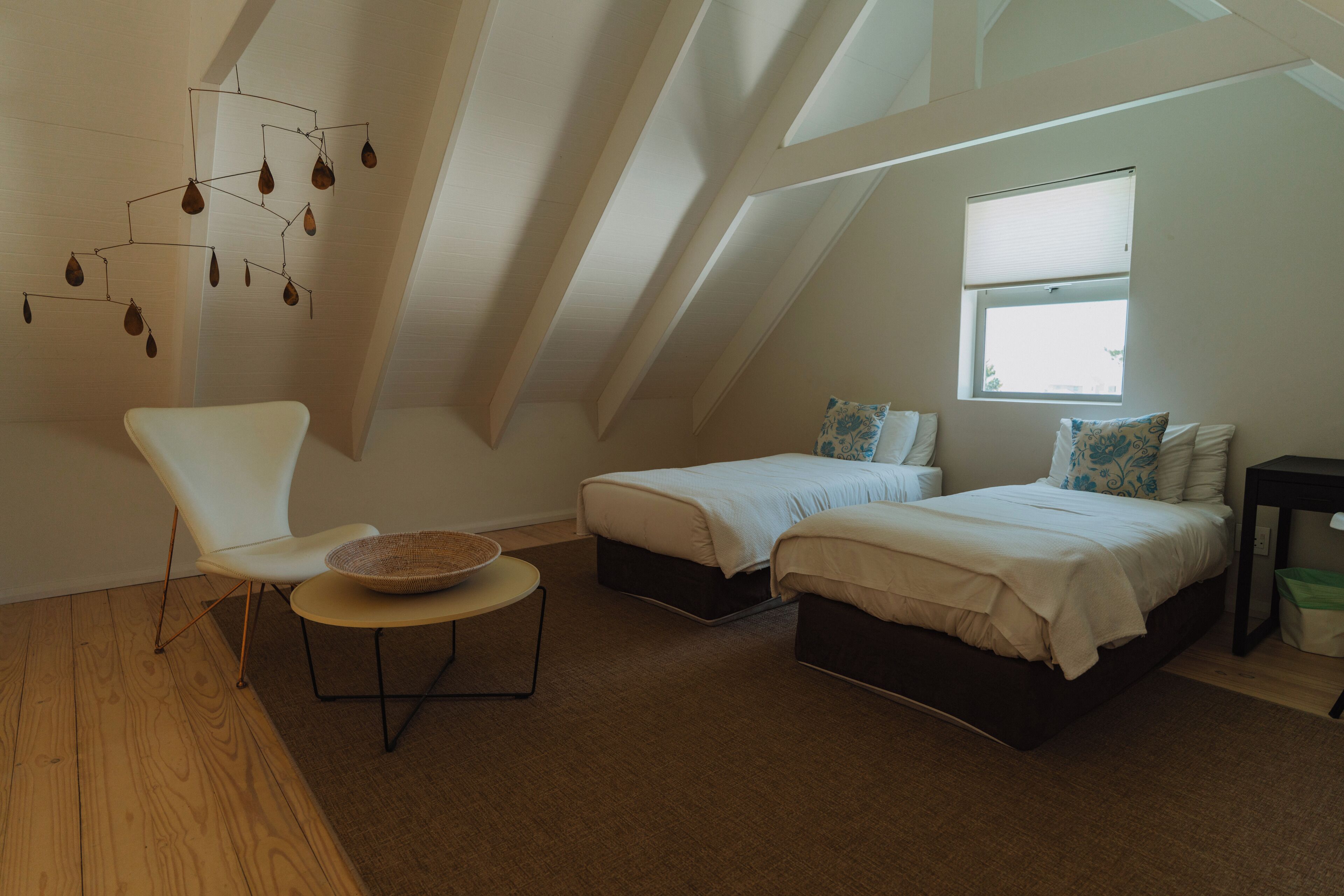 A bedroom with a sloped ceiling, two beds, a chair, a small table, and a decorative hanging light fixture.