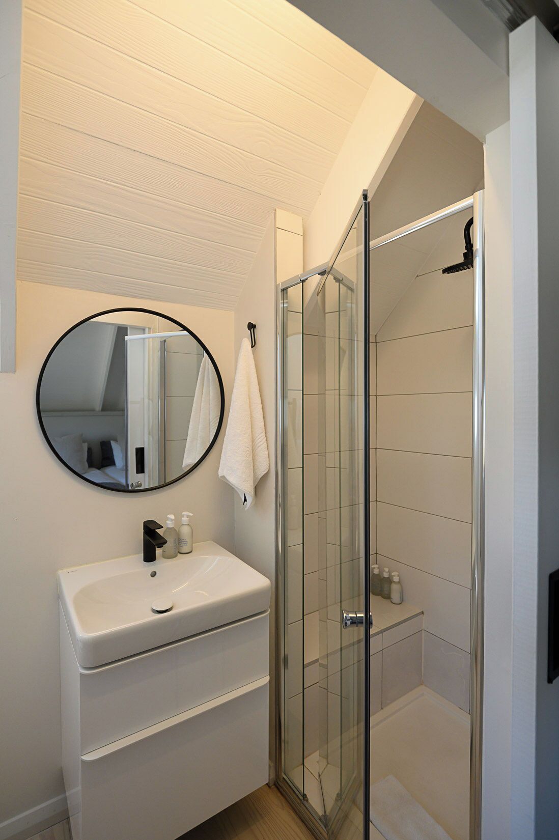 A modern bathroom with a white sink, a round mirror, and a glass-enclosed shower.