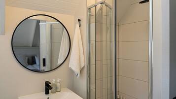 A modern bathroom with a white sink, a round mirror, and a glass-enclosed shower.