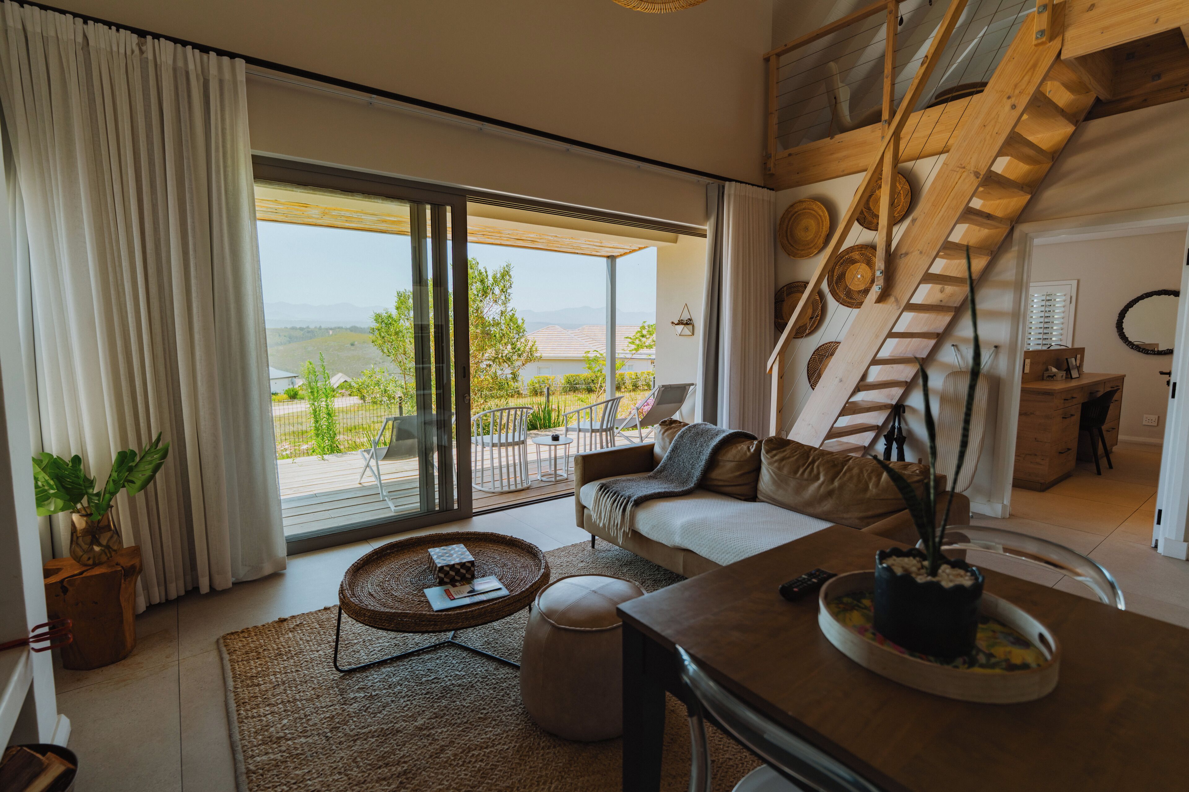 A spacious living area with a large sliding glass door leading to an outdoor patio, a wooden staircase, and a cozy seating arrangement.