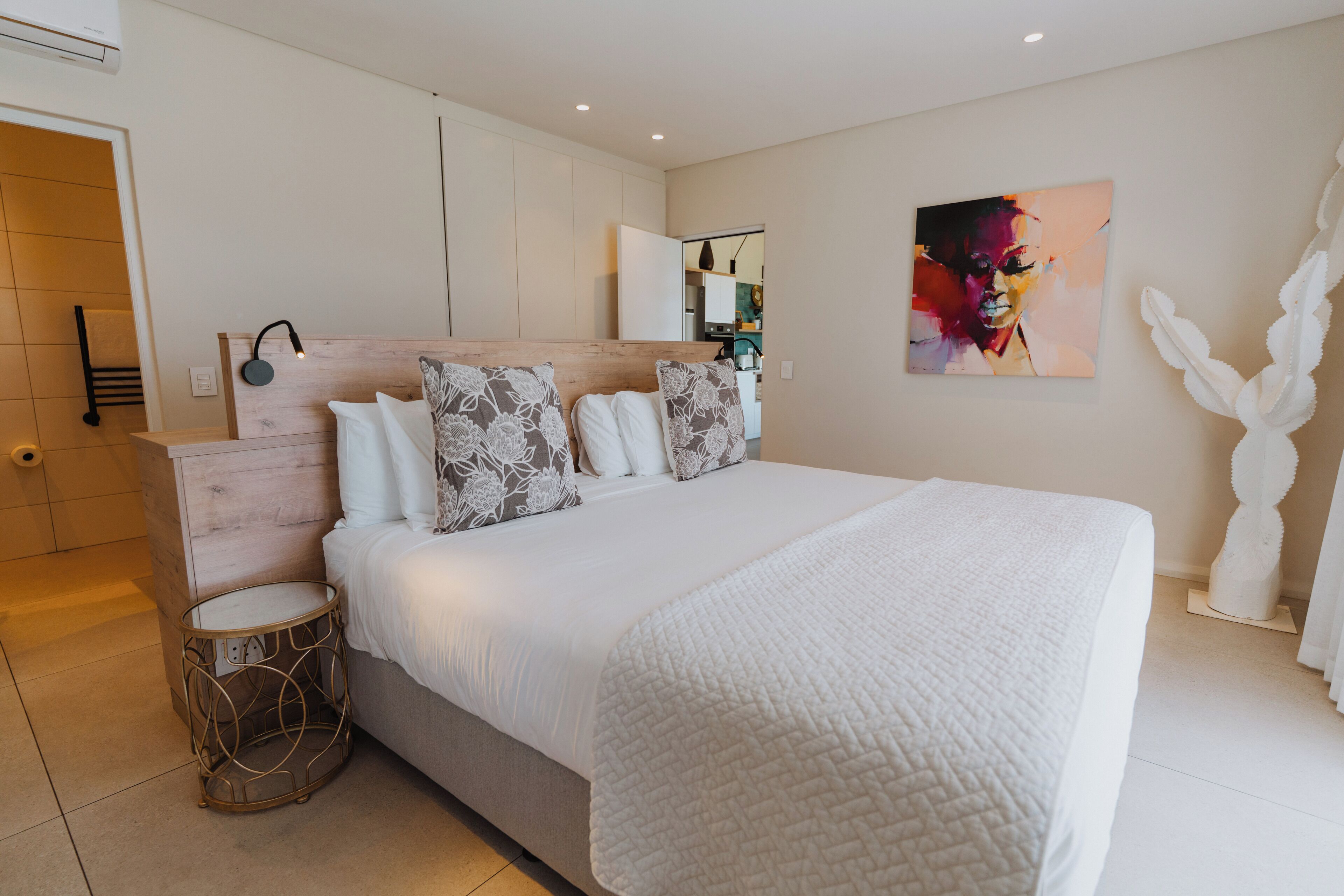Een moderne slaapkamer met een houten hoofdeinde, witte beddengoed en een decoratief schilderij.