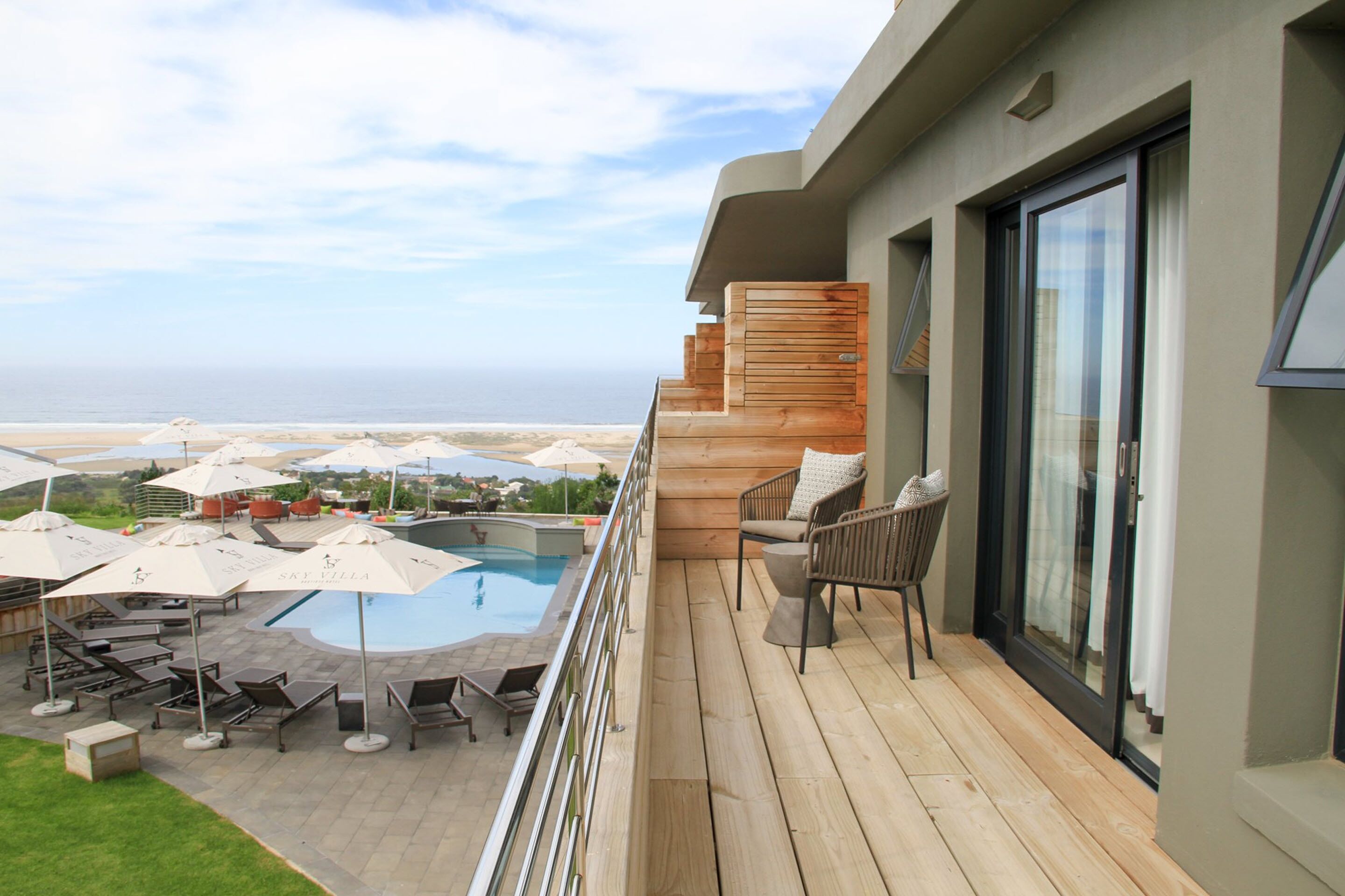 A balcony with a pool, lounge chairs, and umbrellas.
