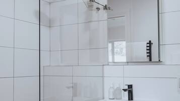 Une salle de bain moderne avec des carreaux blancs, une douche en verre, un lavabo blanc avec un robinet noir et un miroir au-dessus du lavabo.