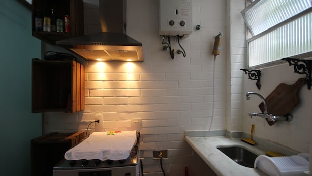 Una cocina con estufa, lavamanos y ventana con persianas.
