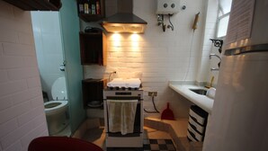 Una cocina compacta con estufa, horno, pileta y una silla roja.