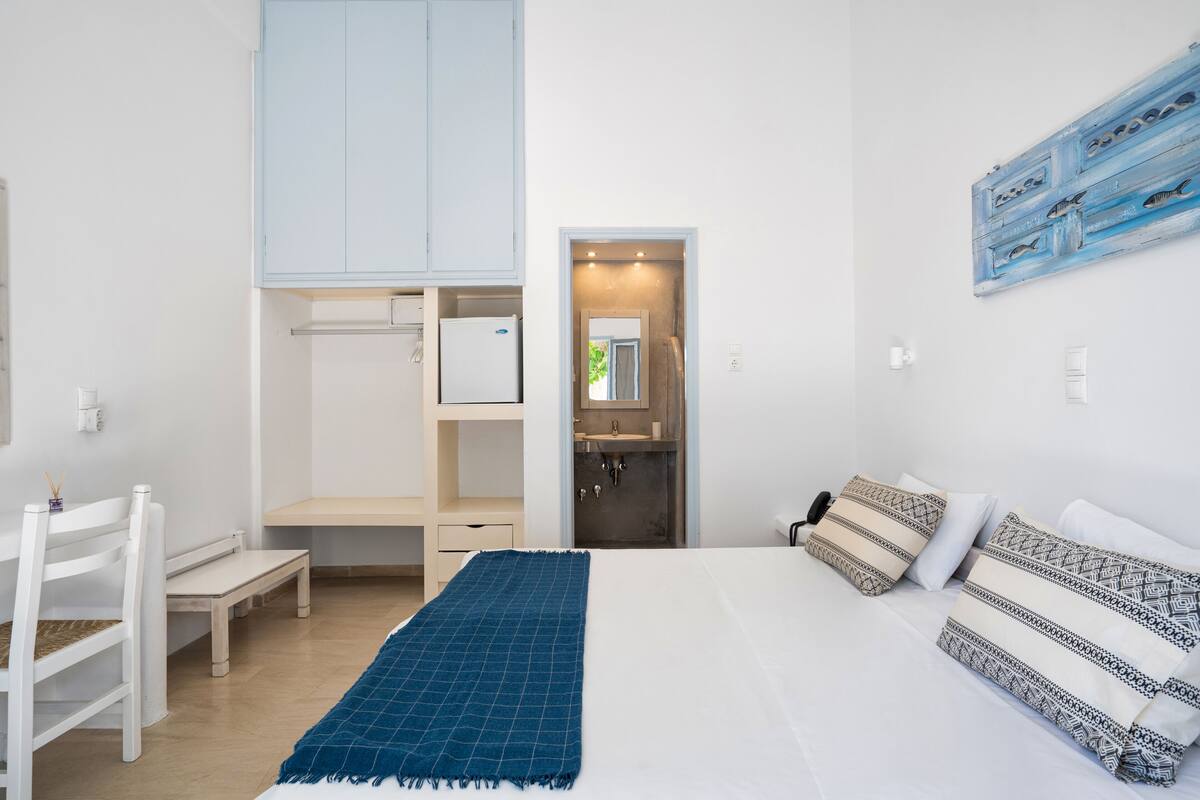 A bedroom with a bed, a desk, a chair, a wardrobe, and a bathroom visible through an open door.
