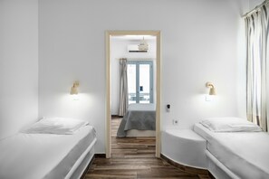Une chambre d’hôtel avec deux lits simples, un plancher en bois, une fenêtre avec des rideaux et une porte donnant sur une autre pièce.