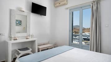 Un dormitorio con cama, escritorio, silla, televisor y ventana con cortinas.