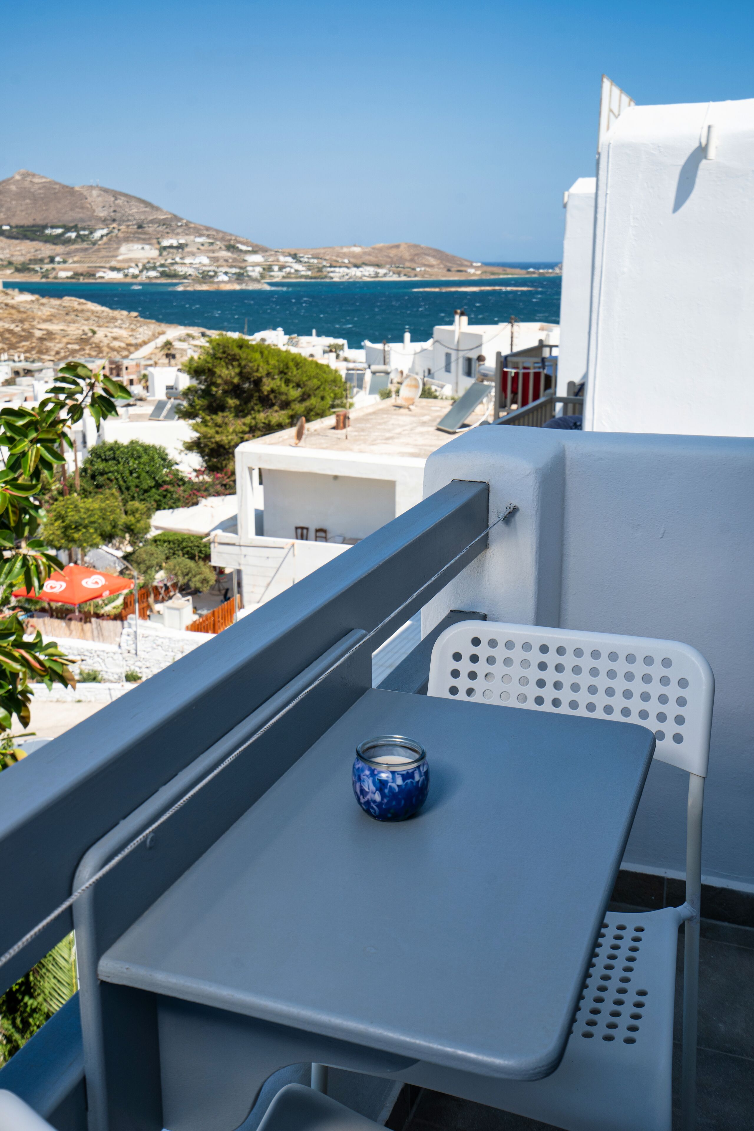 Ein Balkon mit Tisch und einer Dose, mit Blick auf eine Küstenstadt mit weißen Gebäuden und Meerblick.