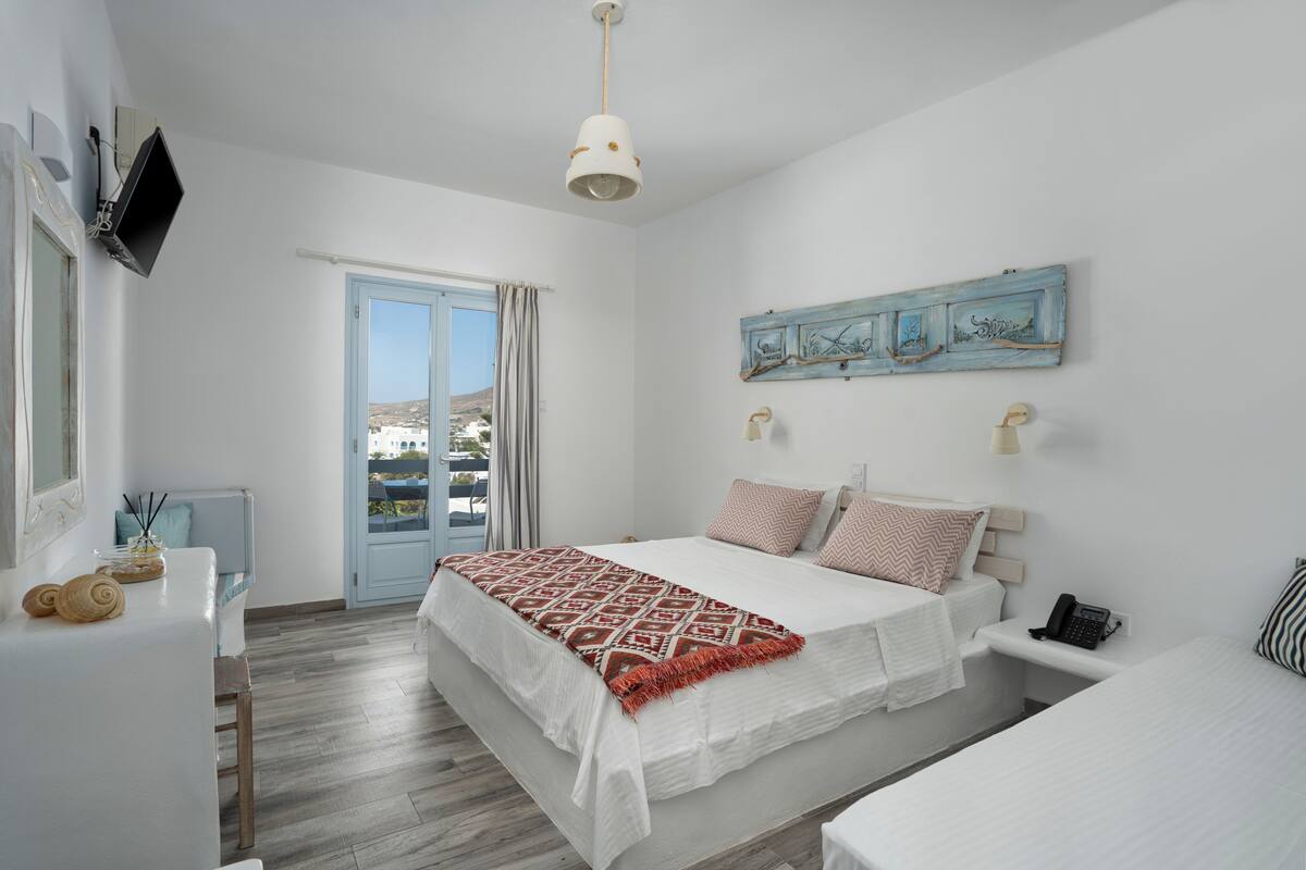 A bedroom with a bed, bedside table, lamp, and a view of the outdoors.