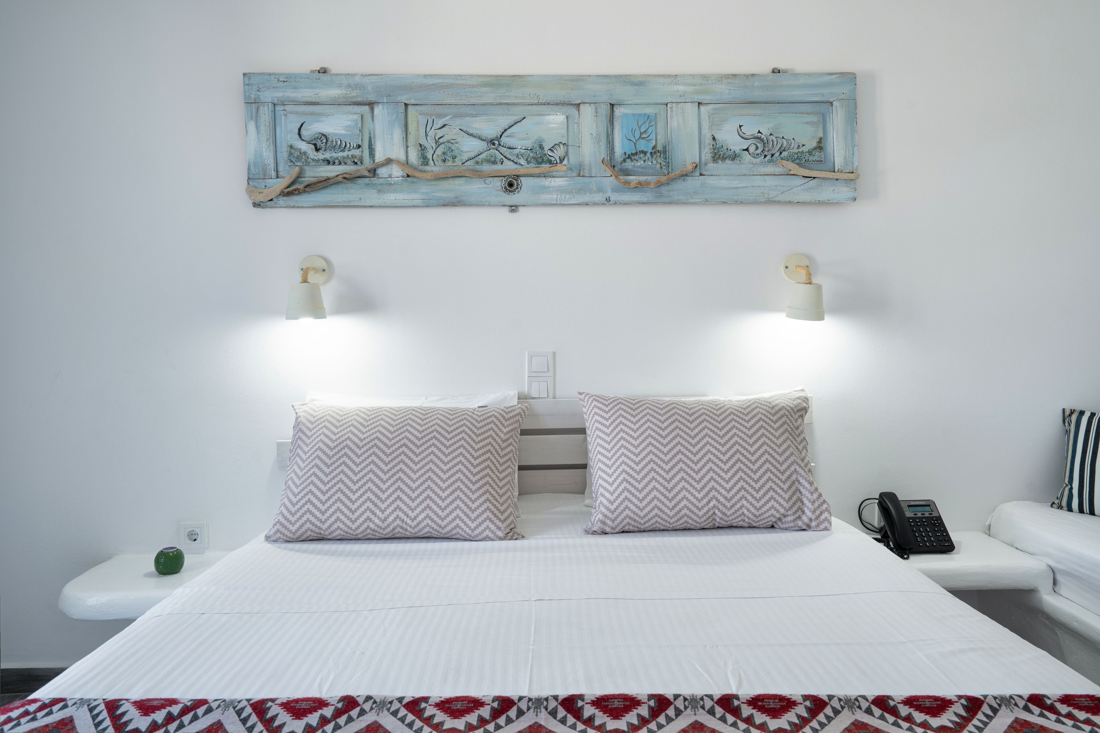 A neatly made bed with patterned pillows, a wall-mounted artwork, bedside lamps, and a phone on the nightstand.