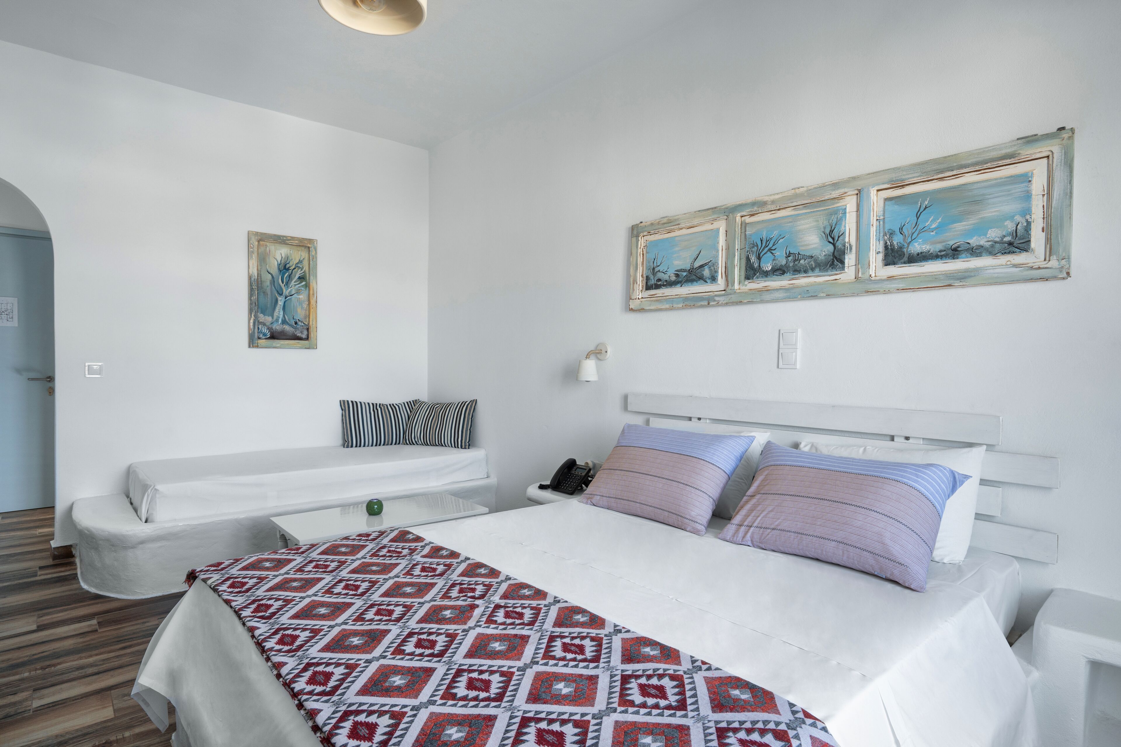 A bedroom with a large bed, two bedside tables, a nightstand, a white sofa, and a wall-mounted telephone.