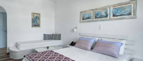 A bedroom with a large bed, two bedside tables, a nightstand, a white sofa, and a wall-mounted telephone.