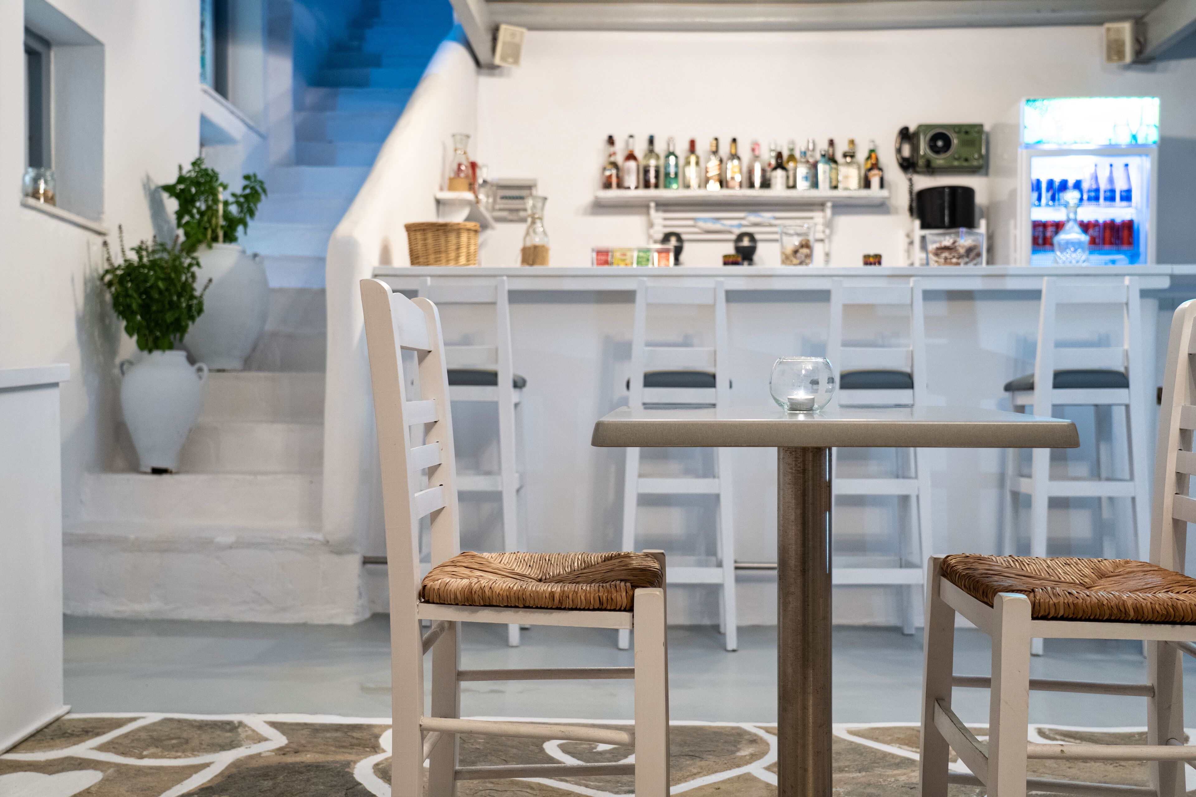 Zona bar con sedie e tavolo bianchi, una scala con pareti bianche e un frigorifero pieno di bottiglie.