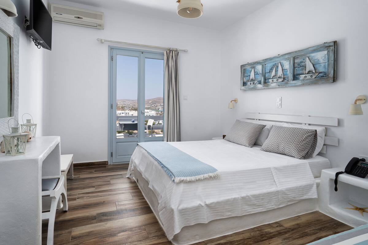 A bedroom with a bed, a desk, a chair, a TV, and a painting of sailboats.
