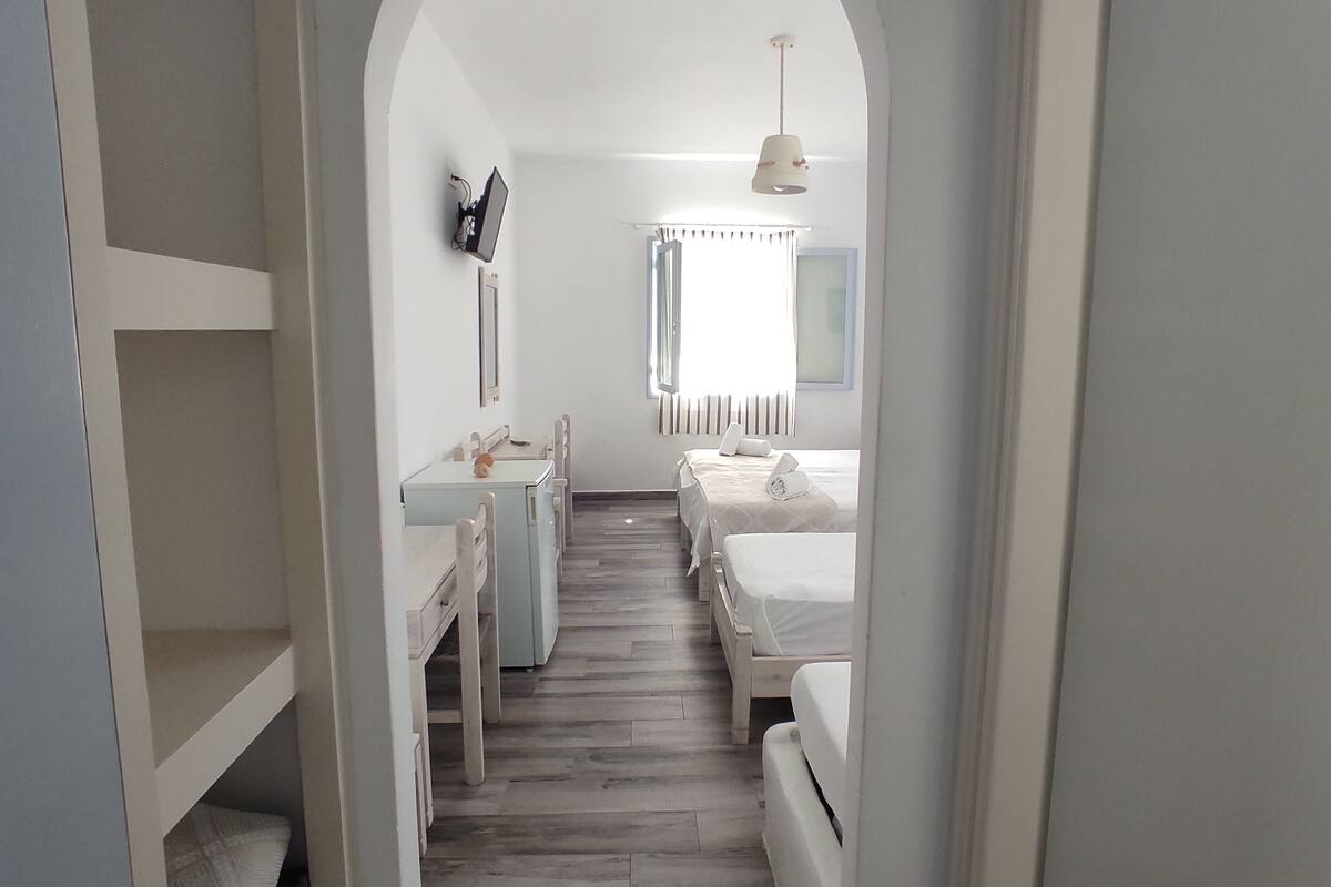A narrow hallway with a wooden floor leading to a bedroom with two beds, a desk, and a chair.