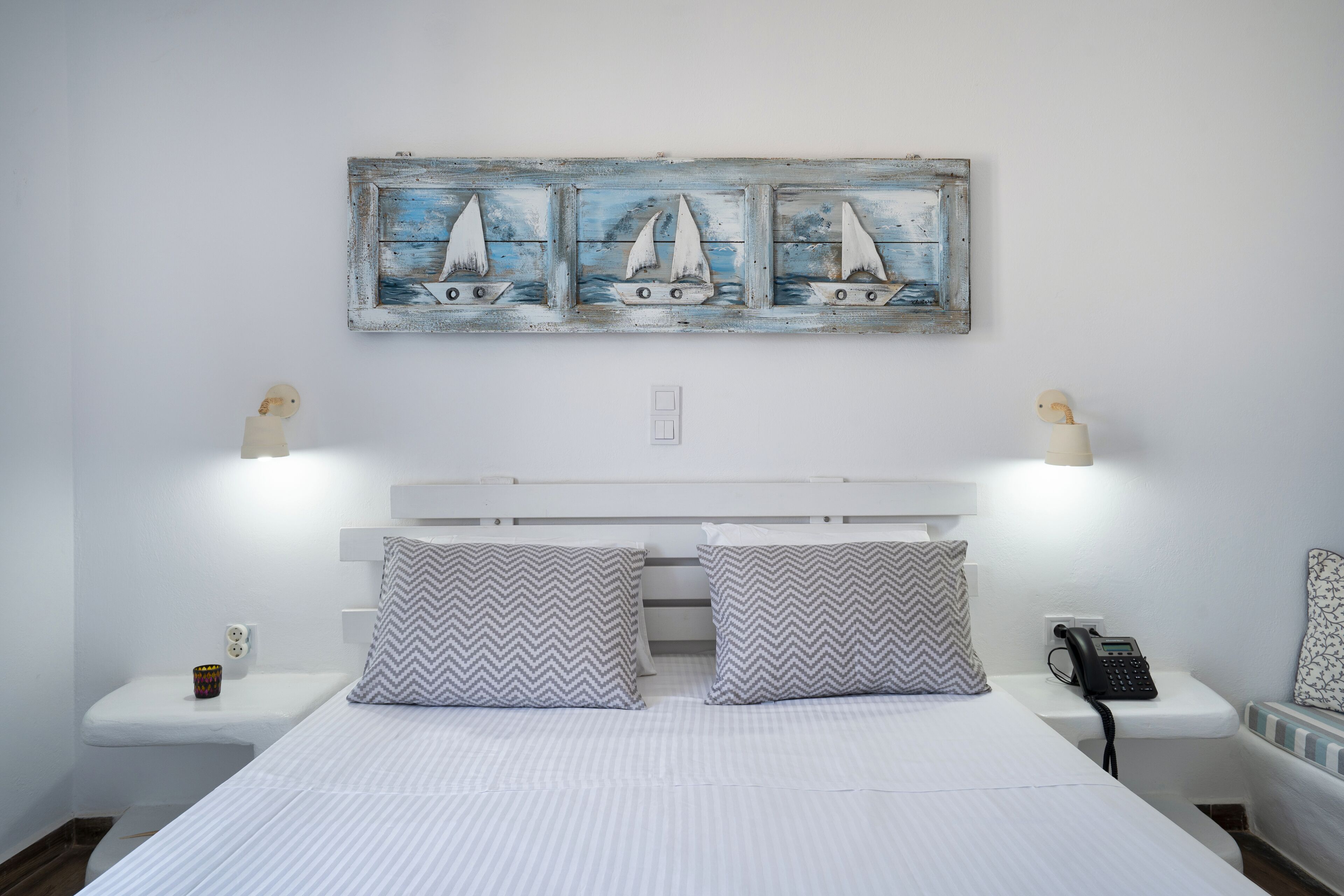 A bedroom with a bed, two nightstands, a wall-mounted phone, and a decorative wall piece above the bed.