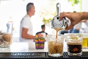 Un barista préparant des boissons à l’aide d’une machine à café, avec un verre rempli de glaçons et une tasse colorée.