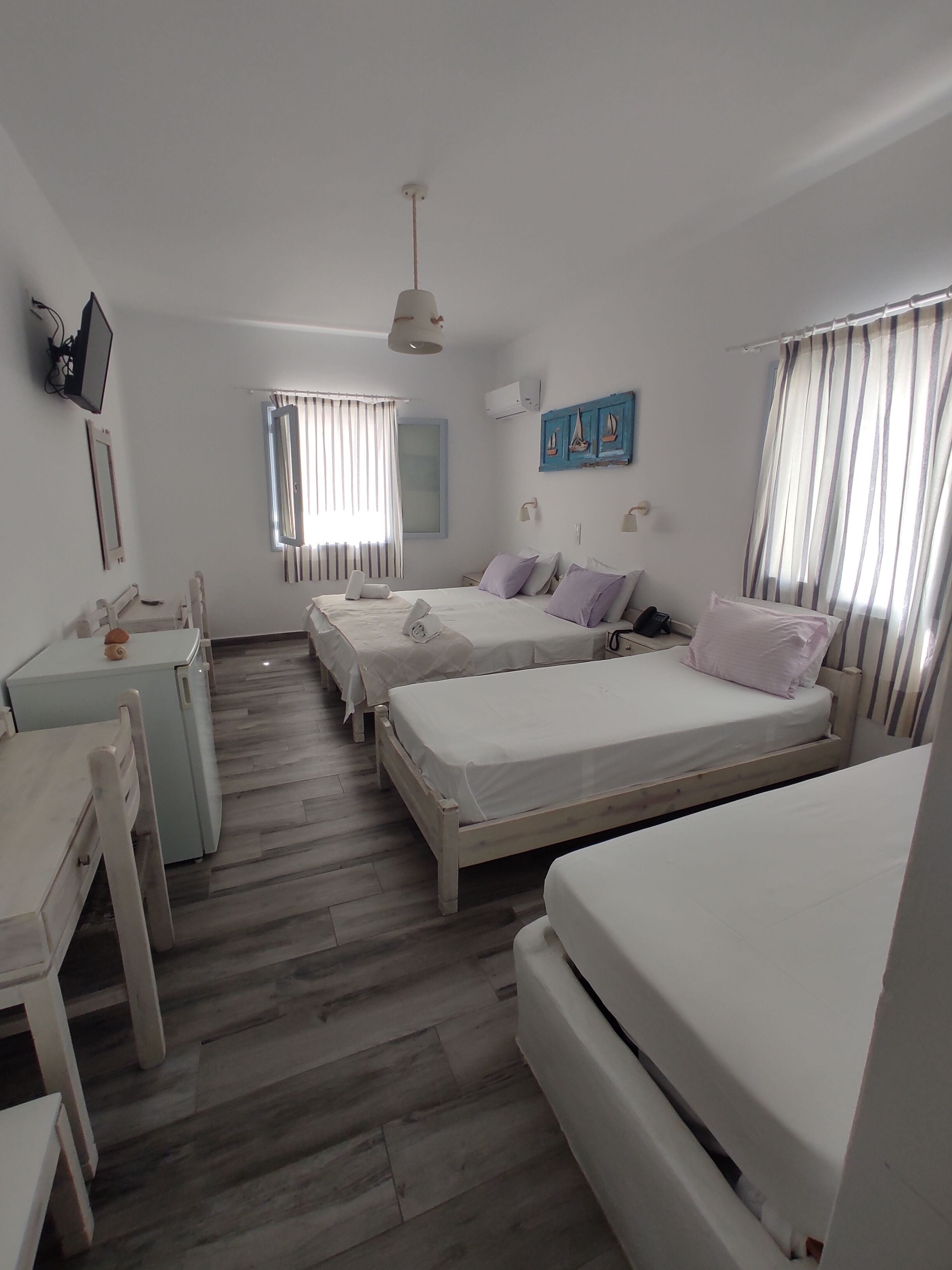 Habitación de hotel con dos camas individuales, un escritorio, una silla, un televisor y una ventana con cortinas.