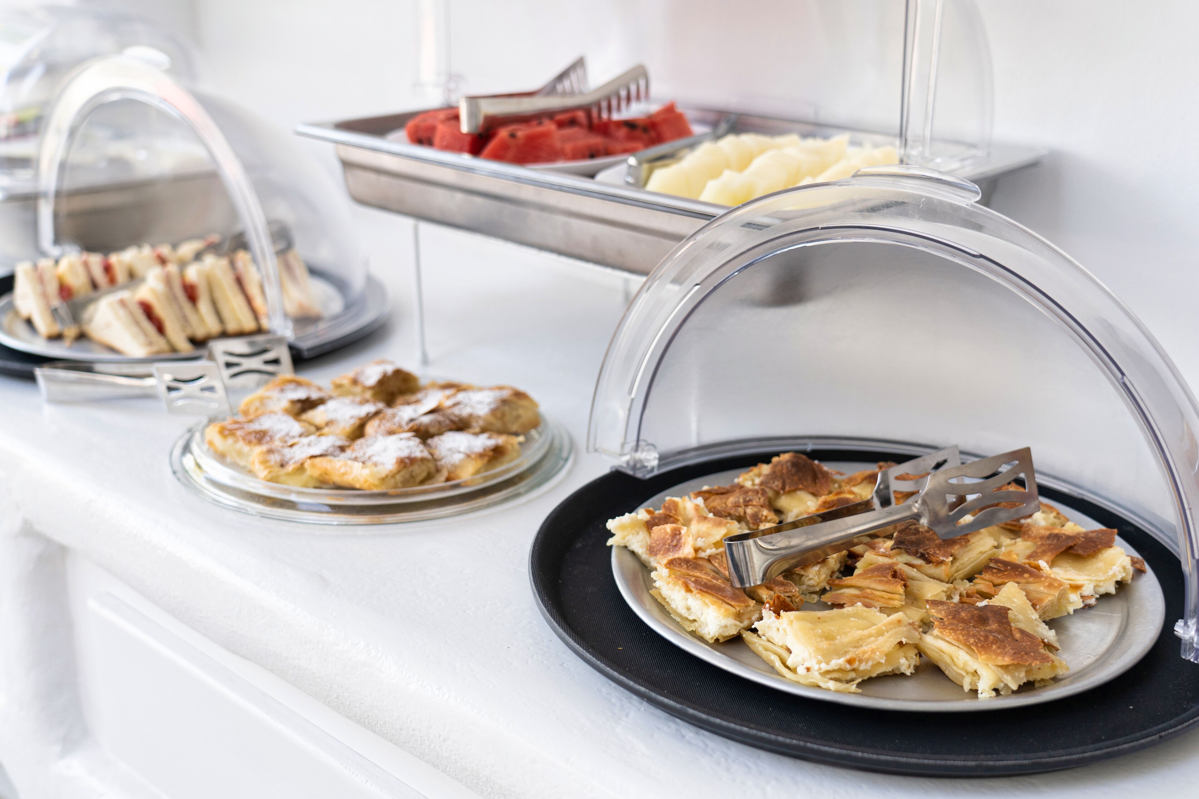 A buffet with various food items, including pastries and fruits, served on clear glass stands.